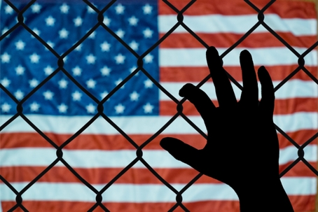 hand on a chain link fence with American flag in the background